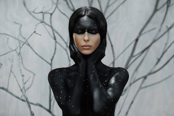 Mysterious woman in black body art portrait with branches background - Фото, изображение