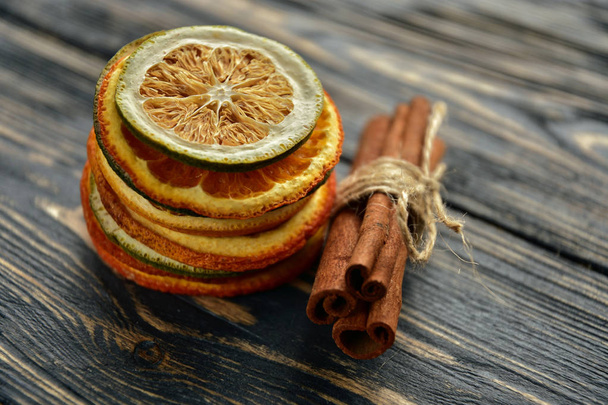 Een stapel gedroogde schijfjes sinaasappel en limoen en kaneelbroodje op een donkere houten achtergrond. Zijaanzicht. Natuurlijk licht. - Foto, afbeelding