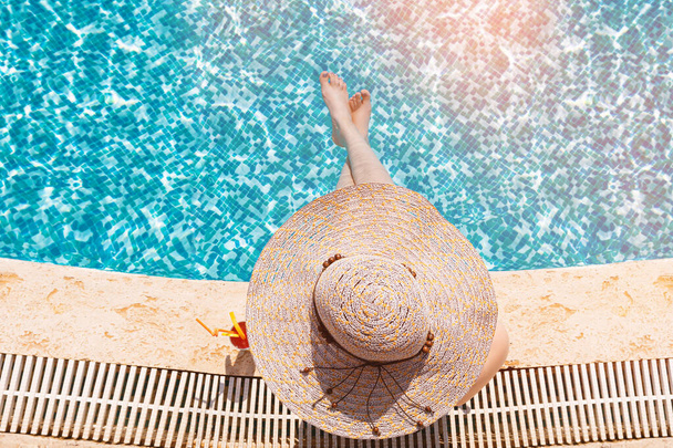Chica joven con sombrero de sol sentado junto a la piscina con cóctel
 - Foto, imagen