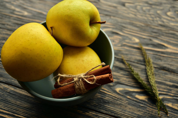Manzanas amarillas y bollo de canela en un tazón sobre un fondo de madera oscura. Vista lateral. Bodegón
. - Foto, imagen