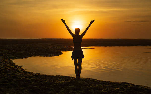 Jeune femme excitée levant les bras à la plage en face de l'océan. Vue de dos. Coucher de soleil heure dorée à la plage. Bali, Indonésie
. - Photo, image
