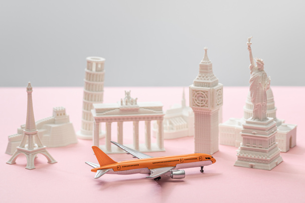 παιχνίδι αεροπλάνο κοντά σε μικρά αγαλματίδια των διαφόρων χωρών σε γκρι και ροζ  - Φωτογραφία, εικόνα