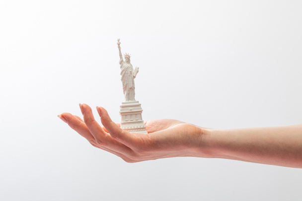 abgeschnittene Ansicht einer Frau mit einer kleinen Freiheitsstatue auf weißem Hintergrund  - Foto, Bild