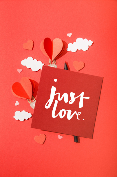 верхний вид бумаги сердечной формы воздушные шары в облаках рядом с карточкой с просто любовь буквы на красном фоне
 - Фото, изображение