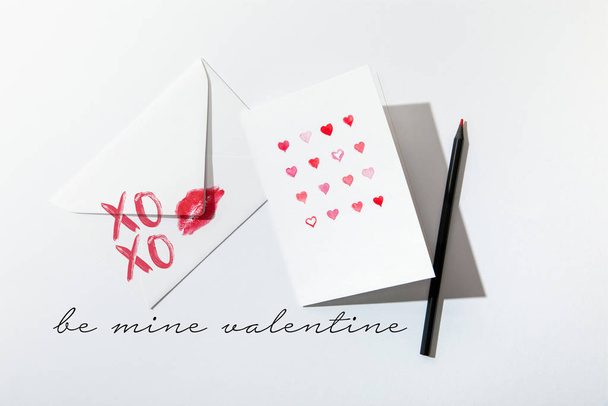 top view of greeting card with hearts near envelope with lip print near be mine valentine lettering on white background - Фото, зображення
