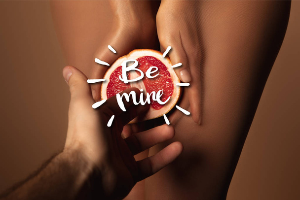 cropped view of man reaching woman in nylon tights holding grapefruit half near be mine lettering on brown - Photo, Image