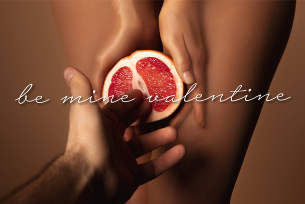 bijgesneden beeld van man bereiken vrouw in nylon panty houden grapefruit half in de buurt van mijn valentijn belettering op bruin - Foto, afbeelding