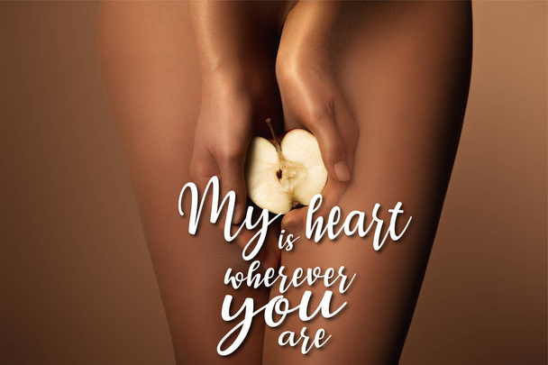 cropped view of woman in nylon tights holding apple half near my heart is wherever you are lettering on brown - Fotoğraf, Görsel