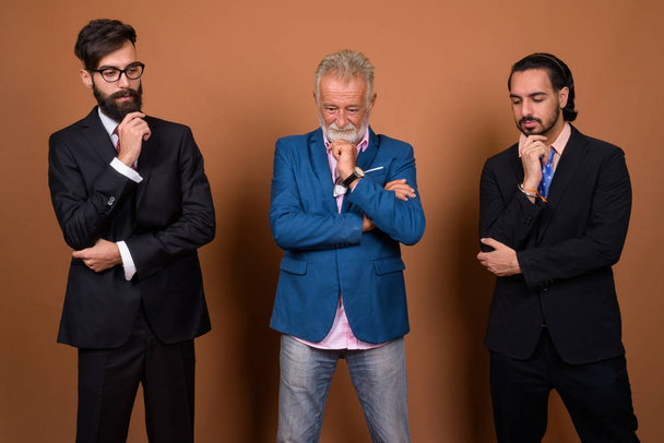 Студійний знімок трьох багатонаціональних бородатих бізнесменів разом на коричневому фоні
 - Фото, зображення