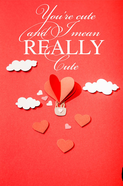 top view of paper heart shaped air balloon in clouds near you're cute and i mean really cute lettering on red background - Foto, Imagen