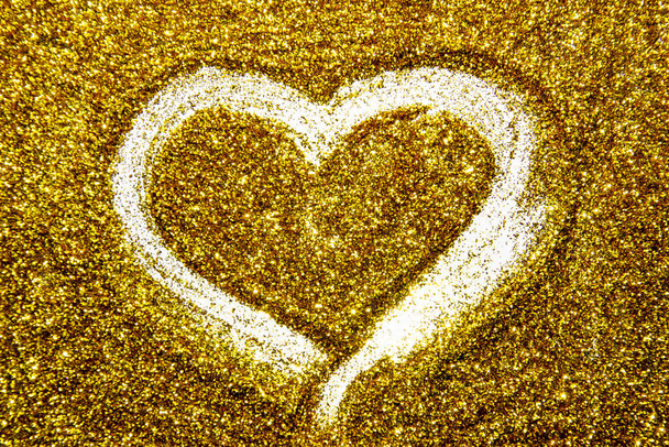 Desenhar um coração no brilho de areia dourada. Um coração contra uma textura dourada no fundo do brilho. Um brilho de ouro brilhante no fundo
. - Foto, Imagem