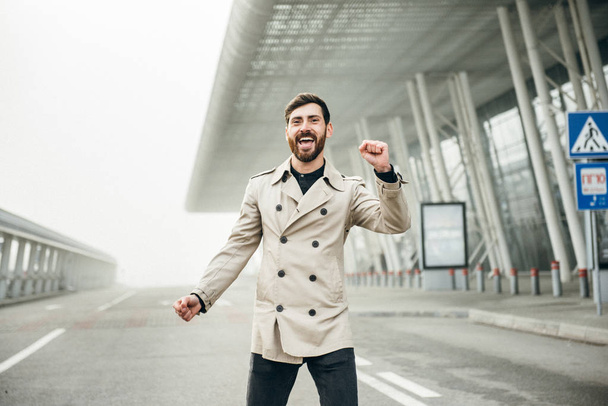 Χαρούμενος και ευτυχισμένος επιχειρηματίας χορεύει ενεργά σε ένα αεροδρόμιο. - Φωτογραφία, εικόνα