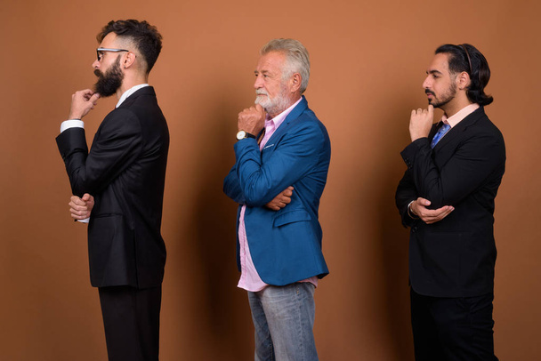 Studio shot of three multi ethnic bearded businessmen together against brown background - Foto, imagen
