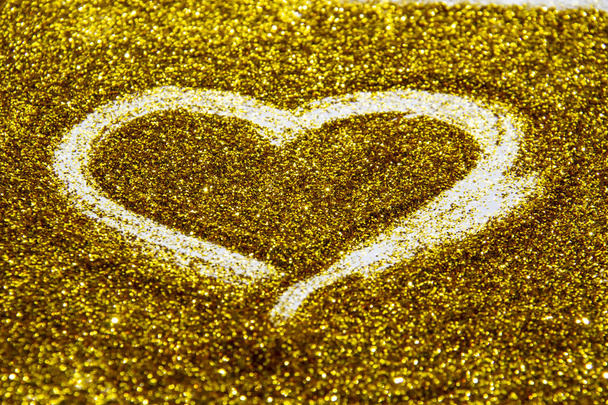 Desenhar um coração no brilho de areia dourada. Um coração contra uma textura dourada no fundo do brilho. Um brilho de ouro brilhante no fundo
. - Foto, Imagem