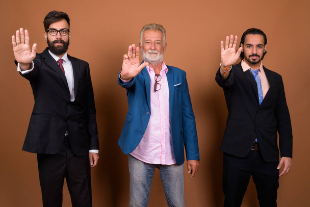 Студийный снимок трех этнических бородатых бизнесменов вместе на коричневом фоне
 - Фото, изображение