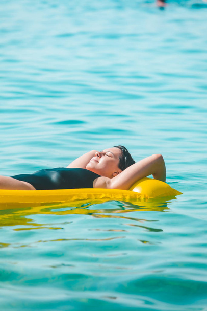 beautiful sexy woman laying on yellow inflatable mattress at sea water - 写真・画像