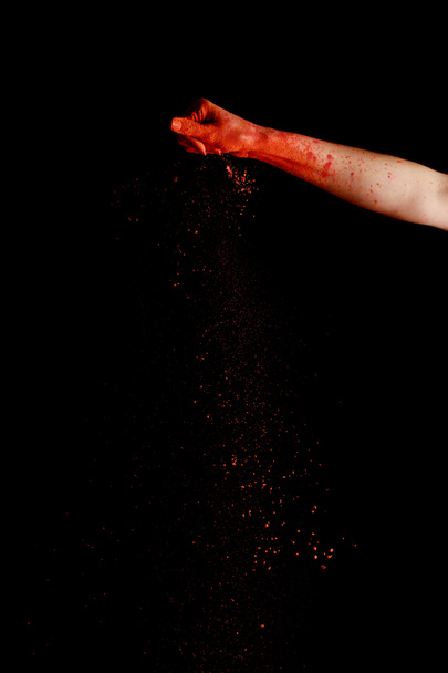mano femenina con polvo de pintura holi colorido rojo sobre fondo negro
 - Foto, Imagen
