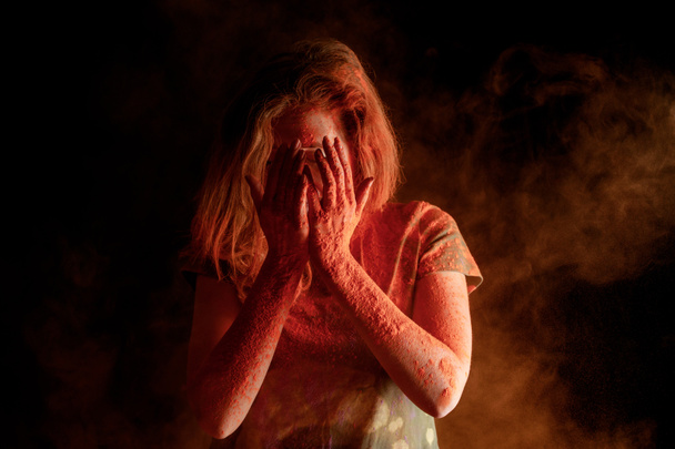 nő borító arc narancs színű holi festék a kezét a fekete háttér - Fotó, kép