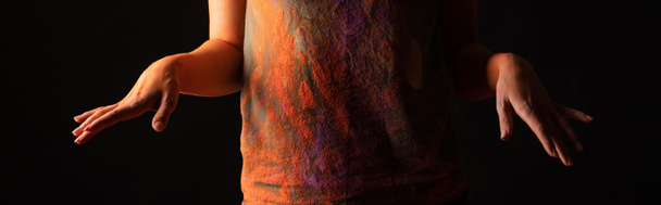 περικοπή άποψη της γυναίκας με πορτοκαλί χρώμα holi σκόνη χρώματος στο σώμα και τα ρούχα που απομονώνονται σε μαύρο, πανοραμική λήψη - Φωτογραφία, εικόνα