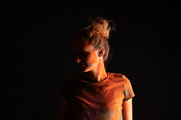 mulher com pó de tinta holi colorido laranja na pele e roupas isoladas em preto
 - Foto, Imagem