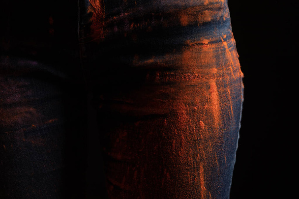 vista recortada de la mujer con polvo de pintura holi de color naranja en jeans aislados en negro
 - Foto, imagen