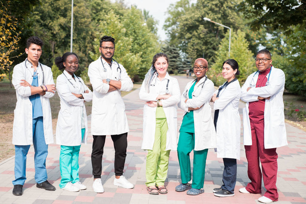 Team gemischter Rennärzte. Gruppe junger Menschen unterschiedlichen Geschlechts in farbiger medizinischer Kleidung, auf der Straße stehend, auf der Straße, mit Phonendoskopen, posierend, lächelnd - Foto, Bild