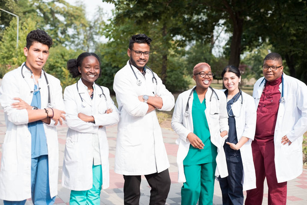 команда врачей смешанных рас. Группа молодых людей разного пола в цветной медицинской одежде, стоящих на улице, на улице, с фонендоскопами, позирующих, улыбающихся
 - Фото, изображение