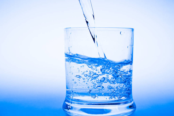 glass of water with splash on blue background - Φωτογραφία, εικόνα