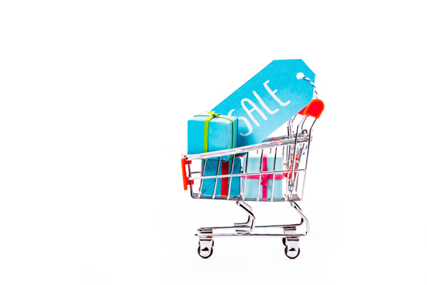 decorative small shopping cart with gift boxes and price tag with sale lettering isolated on white - 写真・画像