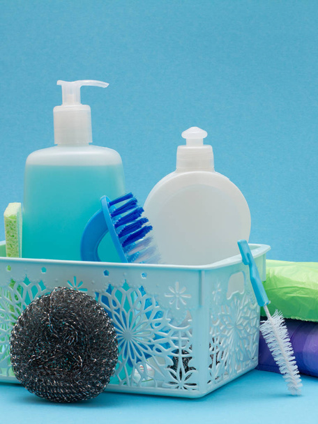 Бутылки жидкости для мытья посуды в корзине, губки и щетки на синем фоне
. - Фото, изображение