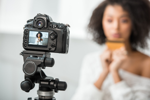 foco seletivo da câmera digital com blogueiro de vídeo afro-americano segurando cartão de crédito em exibição
  - Foto, Imagem