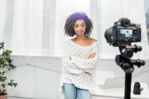selective focus of curly african american influencer standing with crossed arms and looking at digital camera  - Photo, Image