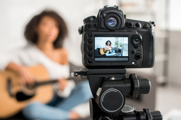 messa a fuoco selettiva della fotocamera digitale con giovane e riccia ragazza africana americana che suona la chitarra acustica in mostra
  - Foto, immagini
