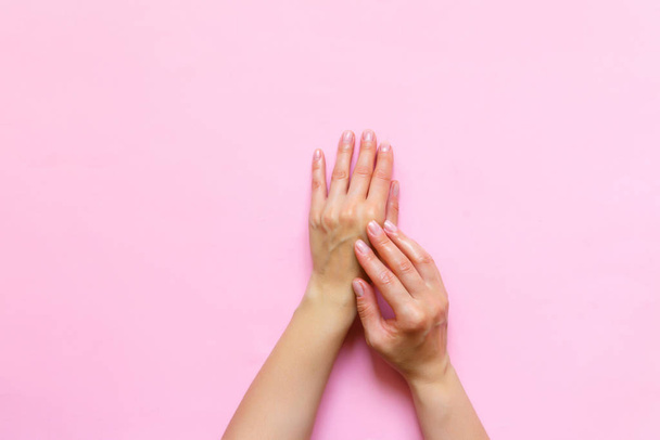 Woman's hands moisturizing cosmetic cream, lotion on a pink background with copy space, beauty, care concept. Pattern flat lay top view - 写真・画像
