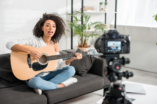 foyer sélectif de la jeune fille afro-américaine dans les accolades jouer de la guitare acoustique et chanter près de l'appareil photo numérique
  - Photo, image