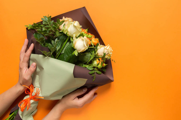 Manos de niña sosteniendo un ramo de rosas sobre un fondo naranja, tarjeta de felicitación, fondo de vacaciones de verano
 - Foto, imagen