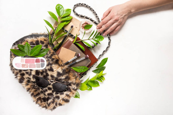 Flat lay set of women's accessories in a bag of fur leopard pattern and tropical leaves on a light background. Fashion, trend and shopping concept - Foto, Imagem