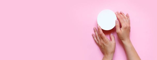 Woman's hands moisturizing cosmetic cream, lotion on a pink background with copy space, beauty, care concept. Pattern flat lay top view long banner - 写真・画像