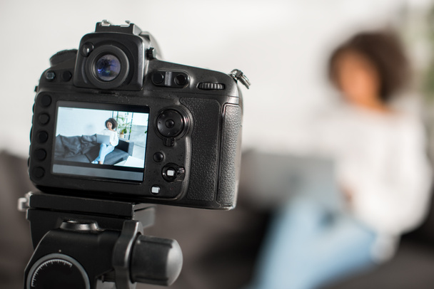 selectieve focus van digitale camera met Afrikaanse Amerikaanse video blogger met behulp van laptop in de buurt van credit card op het display  - Foto, afbeelding