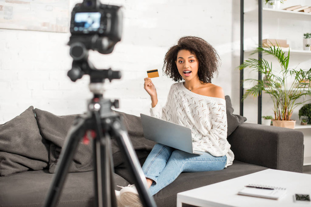 selective focus of african american video blogger holding credit card while shopping online near laptop and digital camera  - Zdjęcie, obraz