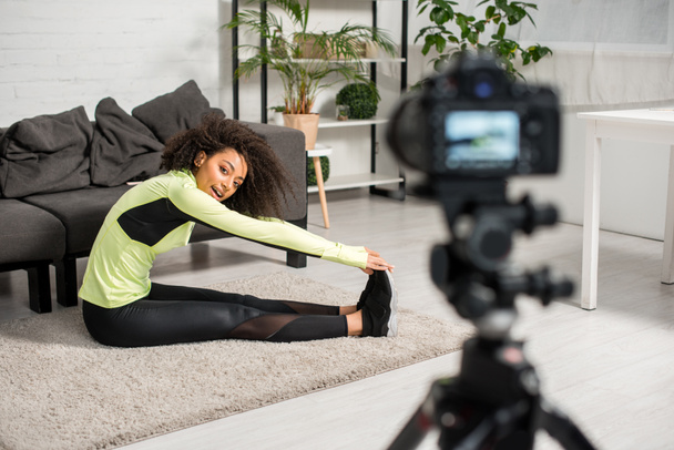 foco seletivo de alegre blogueiro de vídeo afro-americano em aparelhos exercendo perto da câmera digital
  - Foto, Imagem