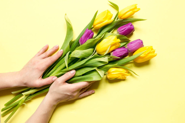 Yellow and purple flowers tulips in a bouquet on a yellow background and the hands of a woman, a festive spring background greeting card - Fotografie, Obrázek