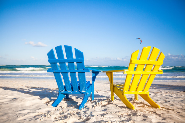 Два деревянных стула: желтый и синий на белом песчаном пляже, Мексика
 - Фото, изображение