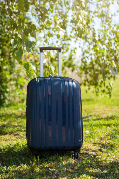 Blue suitcase on the background of nature summer day. Summer concept traveling with a suitcase minimal creative travel concept - Fotó, kép