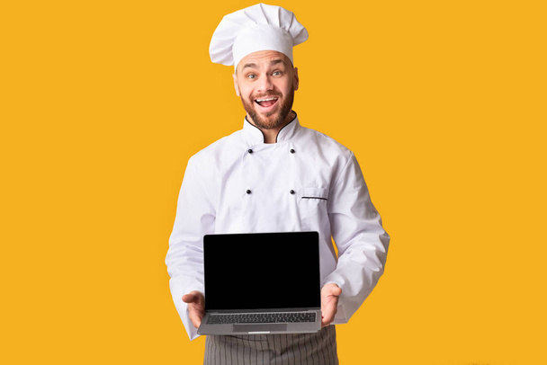 Chef Holding Laptop Számítógép megjelenítése üres képernyő sárga háttér - Fotó, kép