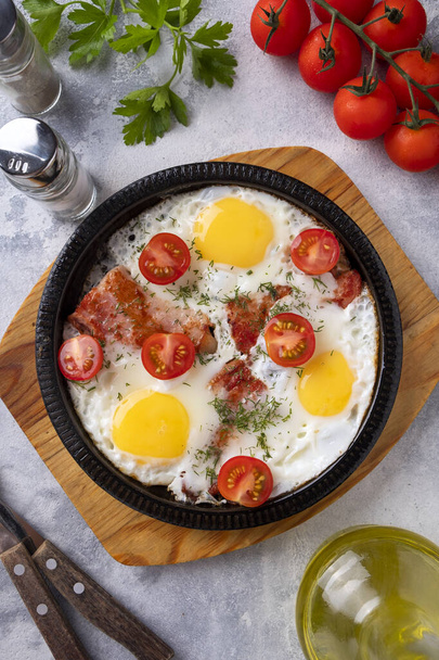 Gefrituurde eieren, spek en groenten op een koekenpan. Ontbijt tijd. Bovenaanzicht.  - Foto, afbeelding