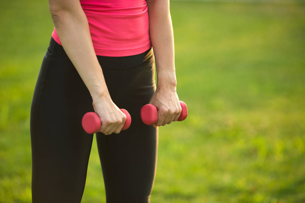 woman with dumbbells in hands in summer park - Photo, Image