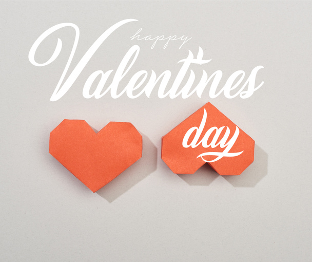 Top view of two red paper hearts on grey background with happy valentines day lettering - 写真・画像