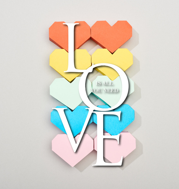 Top view of colorful heart shaped papers on grey background with love is all you need lettering - Photo, Image