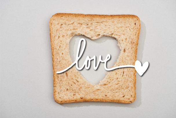Top view of bread slice with carved heart and love lettering on grey background - Foto, Imagen